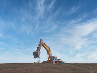 excavator working moving dirt and loading onto a truck with blue sky and clouds