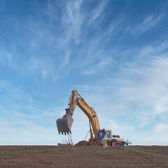 excavator working moving earth and loading on a truck with blue sky and square format clouds
