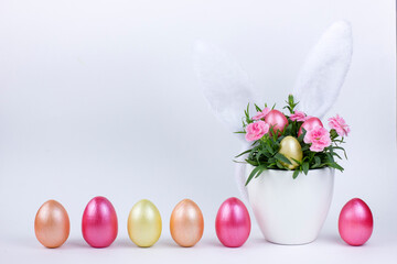 Easter eggs with carnation flower in a flowerpot and bunny ears on a white background.