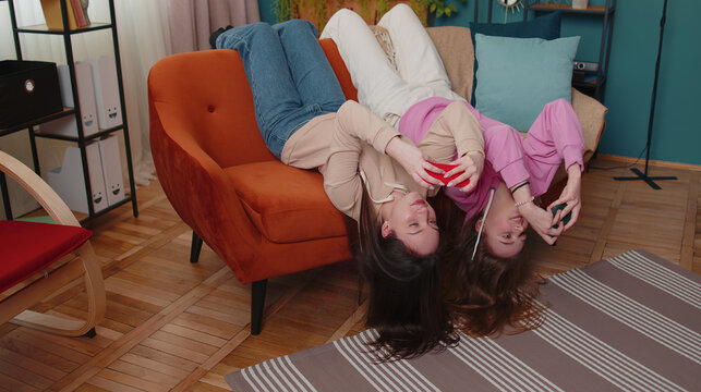 Worried funny girls friends siblings enthusiastically playing racing video games on smartphone. Happy two female women couple family on sofa at home, using smartphone gadget app with drive simulator