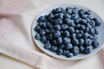 Fresh raw organic blueberries in a plate on a natural linen napkin on the table. Healthy nutrition. Minimalistic simple natural light flat lay template. Superfood. Organic eco health care. Vitamins.