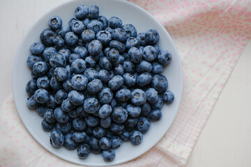 Fresh raw organic blueberries in a plate on a natural linen napkin on the table. Healthy nutrition. Minimalistic simple natural light flat lay template. Superfood. Organic eco health care. Vitamins.