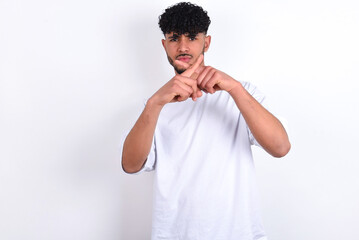 young arab man with curly hair wearing white t-shirt over white background  has rejection angry...