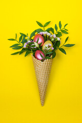 Easter eggs in the waffle cone with spring flowers on yellow background.