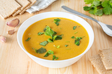Veggie red lentil creamy soup in white bowl on wooden table. Homemade vegan lunch with crispbread.
