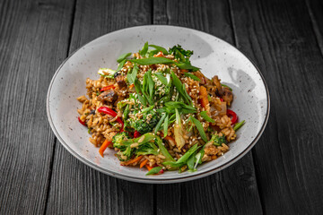 A plate of delicious rice with mushrooms and vegetables: carrots, sweet peppers, greens, spices and sauce on a black background