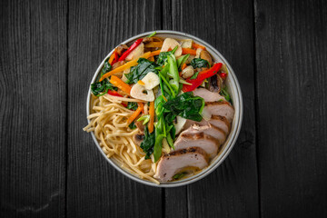 Soba Noodles in broth with chicken fillet, vegetables: carrots, sweet peppers, broccoli on a black background. Sushi menu. Japanese food