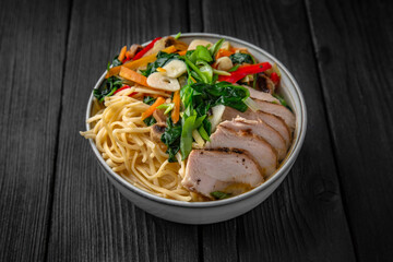Soba Noodles in broth with chicken fillet, vegetables: carrots, sweet peppers, broccoli on a black background. Sushi menu. Japanese food