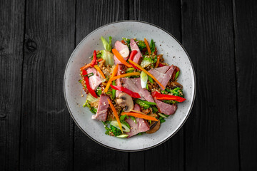 A plate of delicious rice with ham, mushrooms and vegetables: carrots, sweet peppers, greens, spices and sauce on a black background