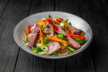 A plate of delicious rice with ham, mushrooms and vegetables: carrots, sweet peppers, greens, spices and sauce on a black background