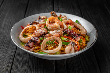 Soba, udon, asian wheat noodles with seafood: shrimps, mussels, squid and vegetables: broccoli, carrots, sweet peppers, zucchini on a black background. Asian style. Japanese food