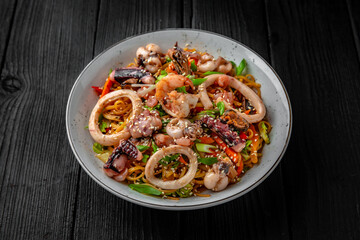 Soba, udon, asian wheat noodles with seafood: shrimps, mussels, squid and vegetables: broccoli, carrots, sweet peppers, zucchini on a black background. Asian style. Japanese food