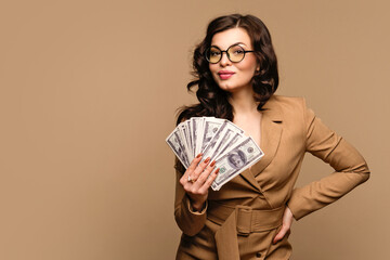 Elegant woman showing fan of cash money in dollar banknotes on beige background. Business, finance, saving, banking and people concept