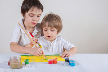 Two children draw together. The senior shows the junior how to draw. The younger one looks intently