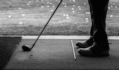 Close-up silhouette of a mans feet and his driver golf club resting on the turf as he practices his...