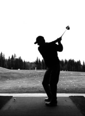 Silhouette of a man mid swing with his driver as he practices golf at a driving range facility...