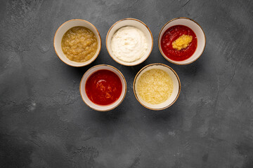 Obraz na płótnie Canvas Set of different sauces in bowls and ingredients on gray rustic concrete background, top view. Tomato ketchup, mayonnaise, guacamole, mustard, soy sauce, pesto, cheese sauce - assortment of dips