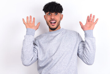 Emotive young arab man with curly hair wearing sport sweatshirt
over white background laughs loudly, hears funny joke or story, raises palms with satisfaction, being overjoyed amused by friend