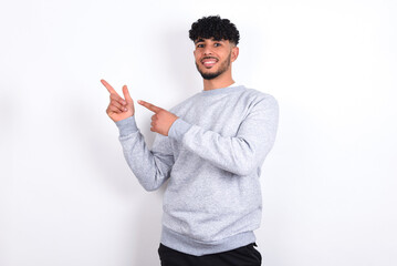 young arab man with curly hair wearing sport sweatshirt
over white background indicating finger empty space showing best low prices, looking at the camera