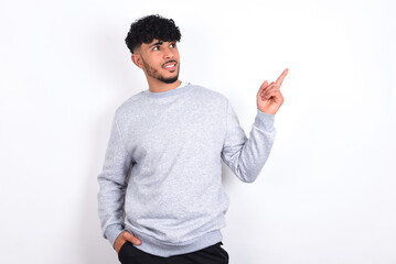 Smiling young arab man with curly hair wearing sport sweatshirt
over white background indicating finger empty space showing best low prices