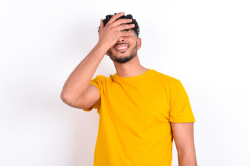 Fototapeta premium young arab man wearing yellow T-shirt over white background smiling and laughing with hand on face covering eyes for surprise. Blind concept.