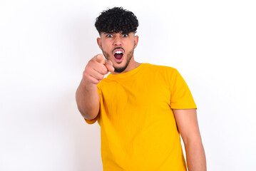 young arab man wearing yellow T-shirt over white background pointing displeased and frustrated to the camera, angry and furious ready to fight with you.