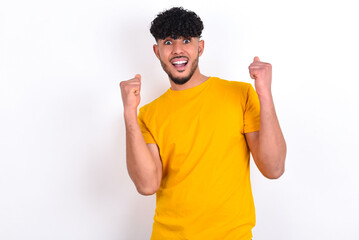 young arab man wearing yellow T-shirt over white background celebrating surprised and amazed for...