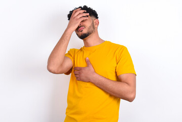 young arab man wearing yellow T-shirt over white background Touching forehead for illness and fever, flu and cold, virus sick.