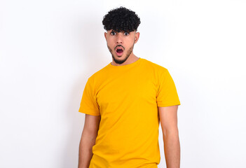 Fototapeta premium Oh my God. Surprised young arab man wearing yellow T-shirt over white background stares at camera with shocked expression exclaims with unexpectedness,