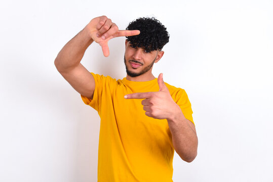 young arab man wearing yellow T-shirt over white background making finger frame with hands. Creativity and photography concept.