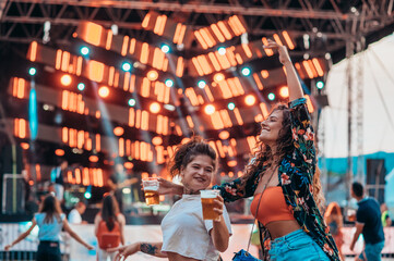 Two beautiful friends drinking beer and having fun on a music festival
