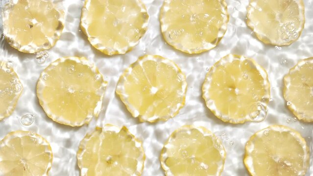 Pouring water splashing and making ripples over lemon slices arranged in lines on white background | beauty product background, cleansing foam commercial