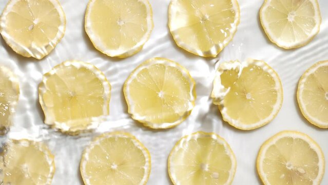 Water waves crossing and splashing over lemon slices arranged in lines on white background | skin care background, peeling commercial