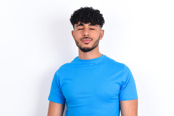 young arab man with curly hair wearing blue t-shirt over white background nice-looking sweet charming cute attractive lovely winsome sweet peaceful closed eyes