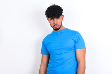 young arab man with curly hair wearing blue t-shirt over white background depressed and worry for distress, crying angry and afraid. Sad expression.