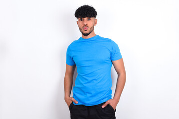 Portrait of lovely funny young arab man with curly hair wearing blue t-shirt over white background sending air kiss