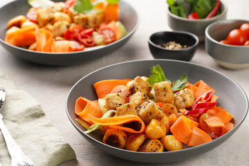 Sweet potato gnocchi with teriyaki tofu with indonesian vegetable salad gado gado - carrots, cucumbers, tomatoes, coriander, sesame seeds and peanut butter dressing in a grey bowl