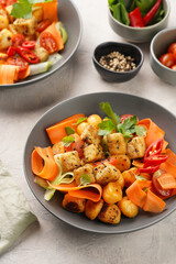 Sweet potato gnocchi with teriyaki tofu with indonesian vegetable salad gado gado - carrots, cucumbers, tomatoes, coriander, sesame seeds and peanut butter dressing in a grey bowl