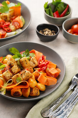 Sweet potato gnocchi with teriyaki tofu with indonesian vegetable salad gado gado - carrots, cucumbers, tomatoes, coriander, sesame seeds and peanut butter dressing in a grey bowl