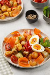 Sweet potato gnocchi with teriyaki tofu with indonesian vegetable salad gado gado - carrots, cucumbers, tomatoes, coriander, sesame seeds, boiled eggs and peanut butter dressing on a white plate