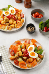 Sweet potato gnocchi with teriyaki tofu with indonesian vegetable salad gado gado - carrots, cucumbers, tomatoes, coriander, sesame seeds, boiled eggs and peanut butter dressing on a white plate