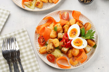Sweet potato gnocchi with teriyaki tofu with indonesian vegetable salad gado gado - carrots, cucumbers, tomatoes, coriander, sesame seeds, boiled eggs and peanut butter dressing on a white plate