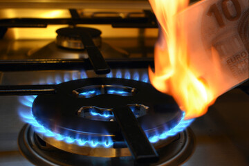 Close-up of a lit gas stove stove with a burning ten euro banknote in foreground