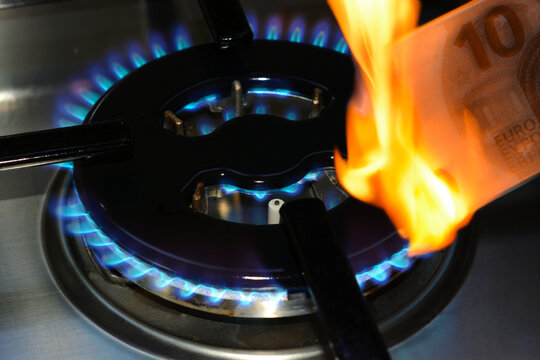 Close-up of a lit gas stove stove with a burning ten euro banknote in foreground