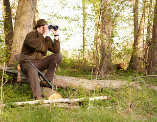 Wildlife hunting requires patience. A game ranger looking through his binoculars while sitting on a...