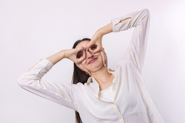 Naklejka premium Close up portrait of attractive quirky young woman making binoculars with hands showing ok gesture on white studio background.