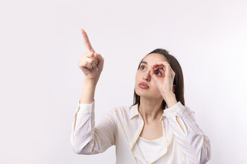 Close up portrait of attractive quirky young woman making binoculars with hands showing ok gesture on white studio background.