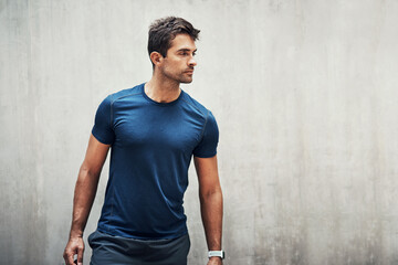Every workout leads to change. Shot of a sporty young man standing against a grey wall while...