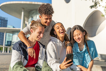 Happy teenage friends looking the cellphone and laughing in the city street. Young people technology concept.