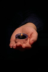 Close-up of a woman's hand holding a burning candle in the dark. Selective focus